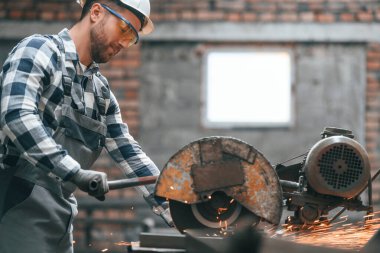 Metali testereyle kesiyorum. Üniformalı fabrika çalışanı içeride..