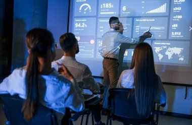 Bilgiyi elden gösteriyor. Erkek lider, borsa şirketinin projektörü çalışanlarla konuşuyor..