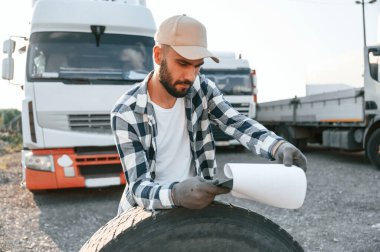Lastiğe yaslanmak, belgeleri okumak. Genç kamyon şoförü gündüz vakti aracıyla geliyor..