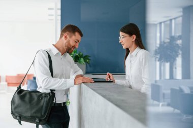 Resepsiyonda. Beyaz gömlekli adam kadının yardımıyla otelde bir oda istiyor..