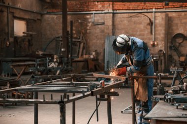 Koruyucu maskeli fabrika işçisi demiri kaynaklıyor..