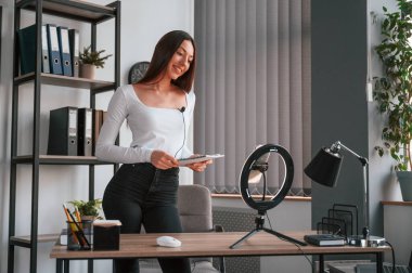 Akıllı telefon kürsüde, kaydediyor. Beyaz elbiseli genç ve güzel bayan ofiste..