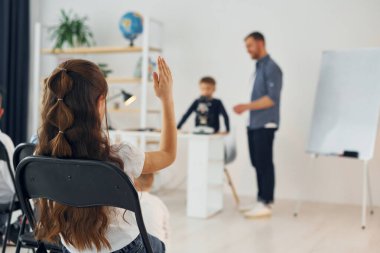 Mikroskobu olan çocuk, kız elini kaldırıyor. Okulda öğretmenle birlikte bir grup çocuk öğrenci..