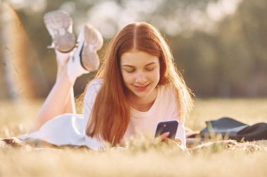 Akıllı telefon kullanıyor. Genç kız güneşli bir günde sahada güzel bir hafta sonu geçiriyor..