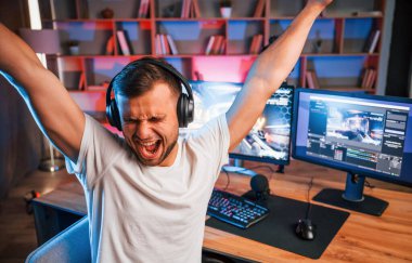 Ellerinizi kaldırın, zaferi kutlayın. Günlük giysiler içindeki erkek oyun flaması içeride bilgisayar ile birlikte..