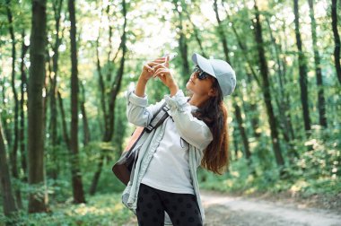 Fotoğraf çekmek için akıllı telefon kullanmak. Kız yaz günü ormanda yeni yerler keşfediyor..