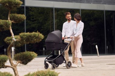 Aşk kavramı. Genç ebeveynler dışarıda bebek arabasıyla geziyorlar..