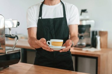 Manzarayı kapat. Bir fincan kahve tutuyorum. Beyaz gömlekli ve siyah önlüklü kafe çalışanı içeride..