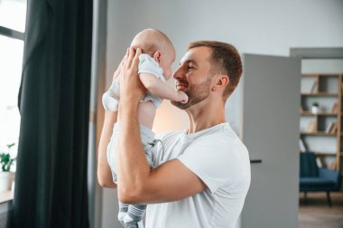 Gülümsemek, bebekle eğlenmek ellerimizde. Bebekli baba evde, oğluyla ilgileniyor..