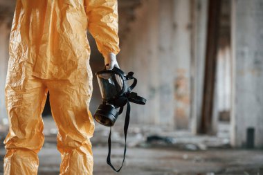 Gaz maskesi tutuyor. Kıyamet sonrası binanın harabelerinde kimyasal koruma kıyafeti giymiş bir adam..