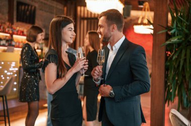 Kadın ve erkek poz veriyor. Güzel giyinmiş bir grup insan içeride yeni yılı kutluyorlar..