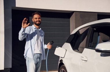 Merhaba, jest. Şarj kablosu duruyor. Genç şık adam, gündüz vakti elektrikli arabayla geziyor..