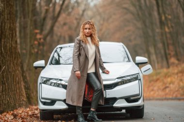 Kadın dışarıda, yolda elektrikli arabasının yanında duruyor..