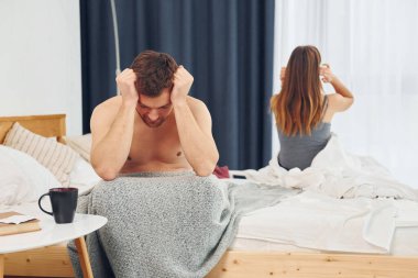 Hayal kırıklığına uğramış bir kadın kendini kötü hisseden bir adamla yatakta oturuyor..