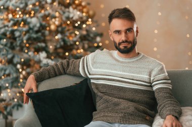 Güzel genç adam yeni yıl gecesi evinde kanepede oturuyor..