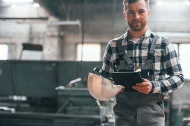 Siyah renkli tablet ellerinde. Üniformalı fabrika çalışanı içeride..