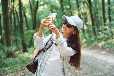 Fotoğraf çekmek için akıllı telefon kullanmak. Kız yaz günü ormanda yeni yerler keşfediyor..