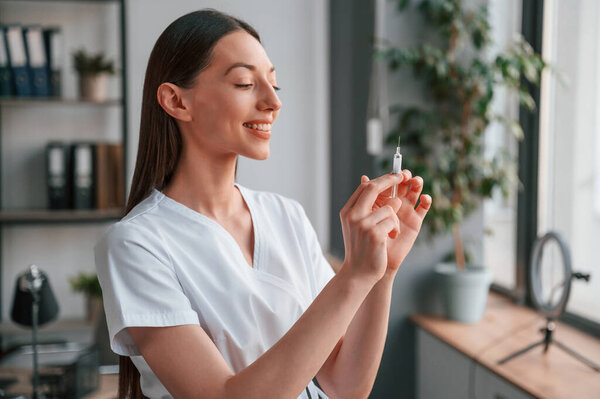 Holding syringe. Young beautiful female doctor in white coat is in the office.
