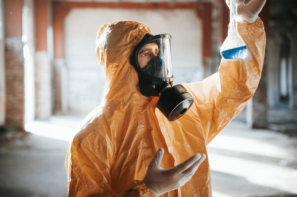 A test tube with radioactive materials. Man dressed in chemical protection suit in the ruins of the post apocalyptic building.