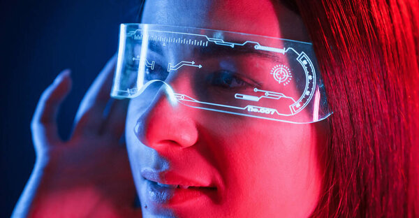 In futuristic eyewear. Young beautiful woman is indoors in the studio illuminated by neon light.