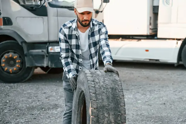 stock image Moving the broken tire. Young truck driver is with his vehicle at daytime.