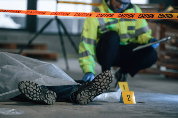 Мужчина-детектив собирает улики на месте преступления рядом с трупом на стройке.