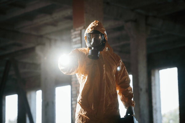 With flashlight. Man dressed in chemical protection suit in the ruins of the post apocalyptic building.