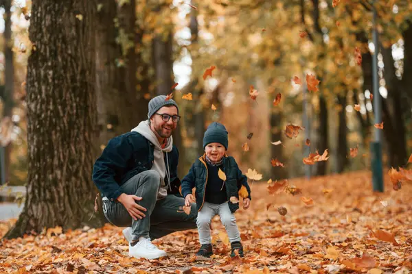 Düşen yapraklarla oynamak. Baba ve küçük oğlu gündüz vakti dışarıda beraberler..