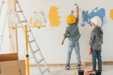 Dikiz aynası. İki çocuk ev odasında duvar boyuyor..