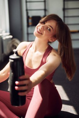 Oturup ara veriyoruz. Spor elbiseli genç bir kadın spor salonunda spor yapıyor..