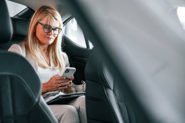 Arka koltukta oturup çalışmak. Beyaz elbiseli kadın araba galerisinde..