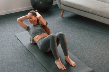 Paspasın üzerinde köpüklü rulo ile. Yoga elbiseli genç bir kadın içeride spor yapıyor..