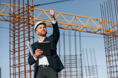 El hareketleriyle emirler veriyor. Resmi kıyafetli bir işadamı gün içinde şantiyede olacak..