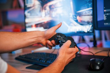 Oyun kumandası ile ellerin görüntüsünü kapat. Günlük giysiler içindeki erkek oyun flaması içeride bilgisayar ile birlikte..