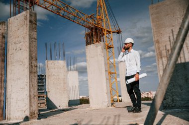 Telefonla konuşmak ve belgeleri elinde tutmak. Üniformalı adam inşaat alanında çalışıyor..