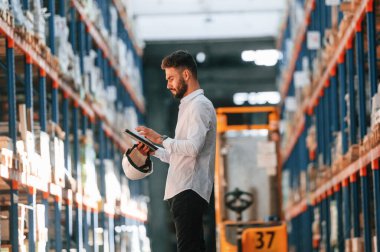 Elinde tabletle. Depo işçisi depoda bir sürü ürünle birlikte..