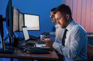 Akıllı telefonu elinde tutarak. Ofiste değişim teknolojisiyle çalışan iki borsacı..