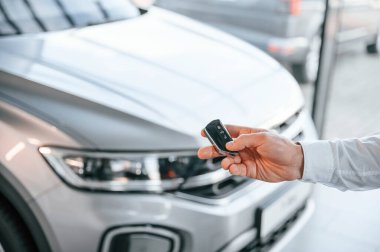 Anahtarlar ve uzaktan kumanda. Manzarayı kapat. Beyaz elbiseli genç adam araba galerisinde..