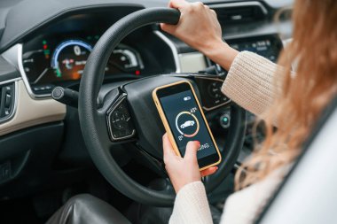 Direksiyon başında oturmak ve şarj işlemini gösteren akıllı telefonu tutmak. Genç bayan otomobilde..