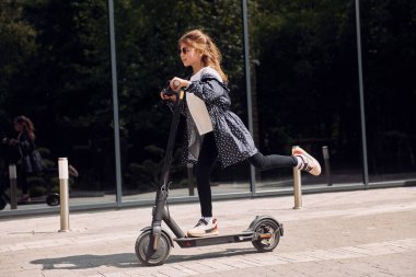 Yan görüş. Küçük kız açık hava binasının yakınında motosiklete biniyor..