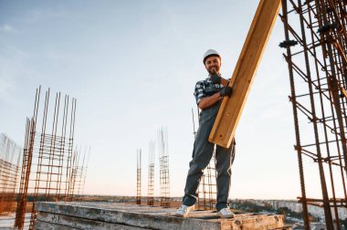 Gri üniformalı. Tahta tutuyorlar. Gündüz vakti inşaatta çalışan bir adam var..