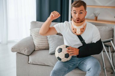 Oturmak, futbol topu tutmak, maç izlemek. Koltuk değnekli adam evde. Yaralı..