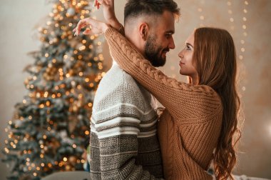 Yan görüş. Ayakta durmak ve birbirimizi kucaklamak. Güzel genç çift yeni yılı evde kutluyor..