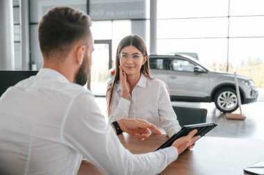 Neşeli müşteri gülümsüyor. Beyaz elbiseli bir adam araba galerisinde birlikte..