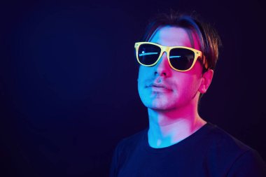 In yellow sunglasses. Man standing in the studio with neon light.