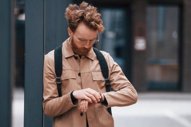 Saatlere bakıyorum. Sakallı, haki renkli ceketli ve kot pantolonlu şık bir adam binanın yanında..