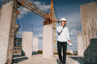 Telefonla konuşmak ve belgeleri elinde tutmak. Üniformalı adam inşaat alanında çalışıyor..