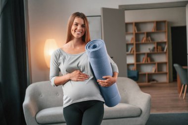 Mavi renkli yoga minderi hazır. Güzel hamile kadın evde..