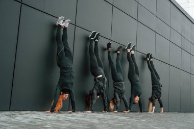 Amuda kalkmak. Bir grup sportif kadın dışarıda, siyah binanın yakınında..