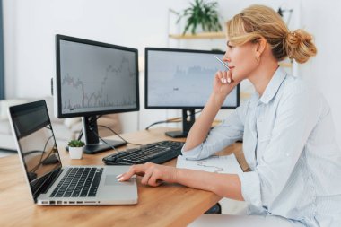 Yan görüş. Resmi giyimli kadın borsacı ofiste çalışıyor..